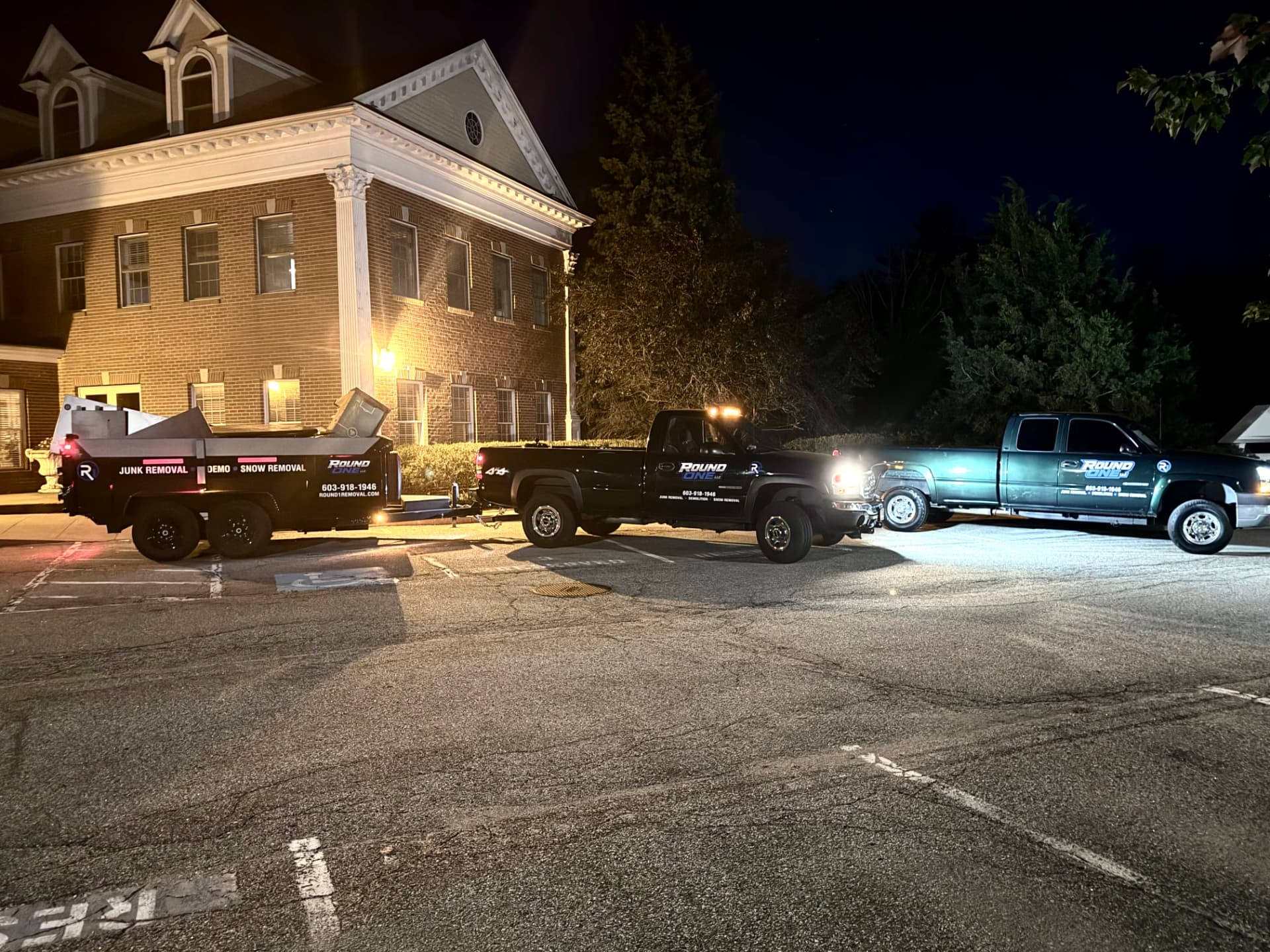 Round One Removal trucks and a loaded dump trailer parked at night in Hampton, New Hampshire